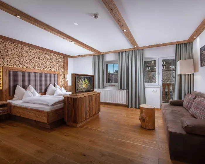 Schlafzimmer mit großem Doppelbett, Couch und Fernseher, mit vielen natürlichen Holzmaterialien