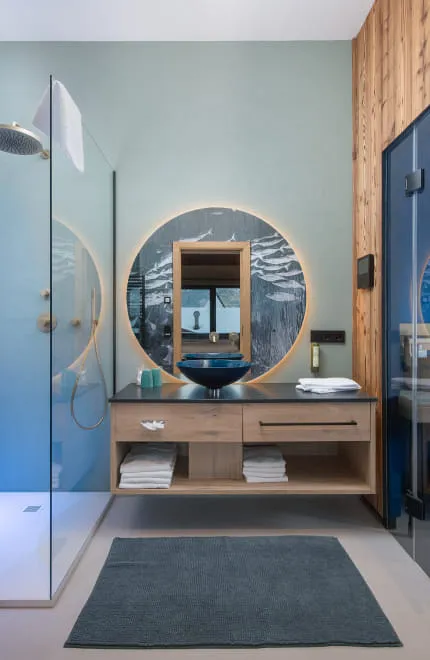 Modernes Badezimmer mit rundem, großem Spiegel und angrenzender Sauna